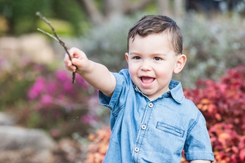 Young mixed race aboriginal caucasian boy playing with stick in garden