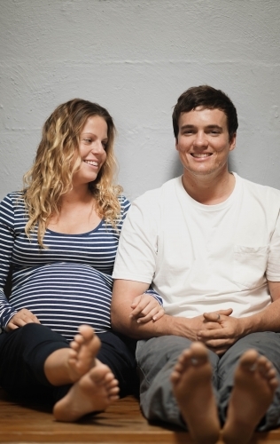 Young pregnant couple sitting against white wall