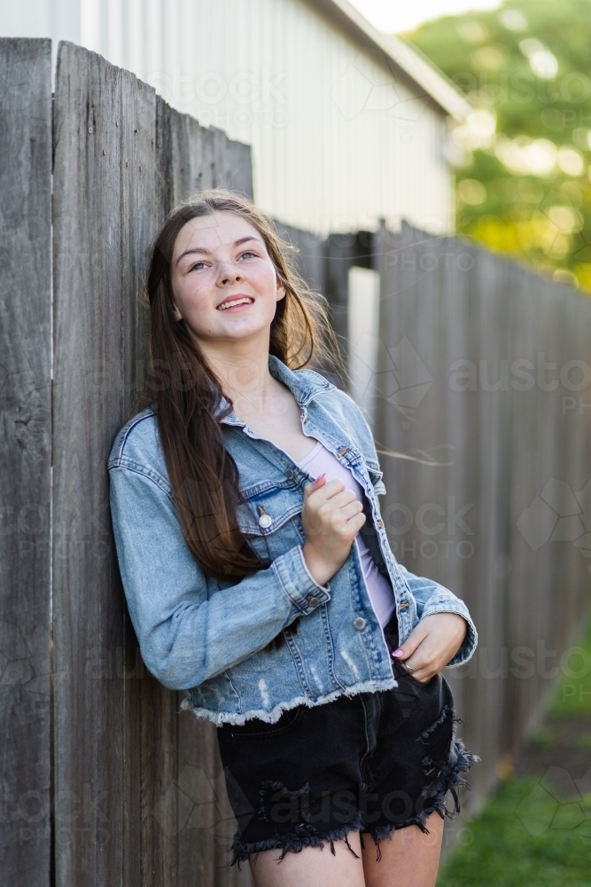 14yo girl leaning on fence looking up dreamily - Australian Stock Image