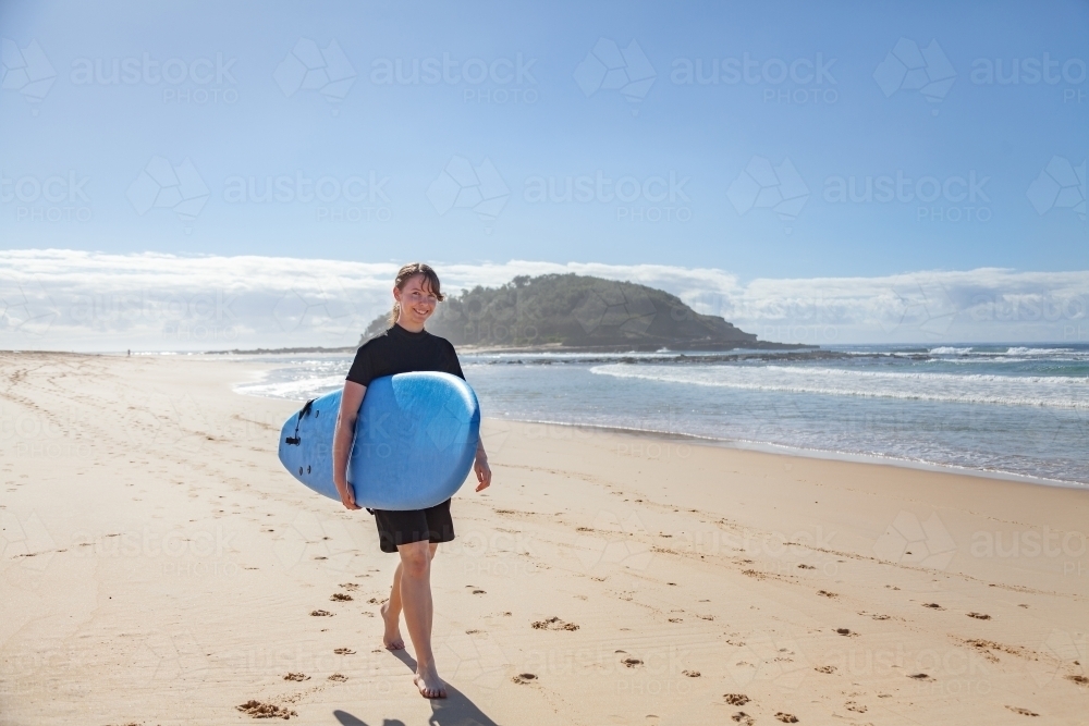 16 year old girl carrying a surfboard down the beach to the ocean - Australian Stock Image