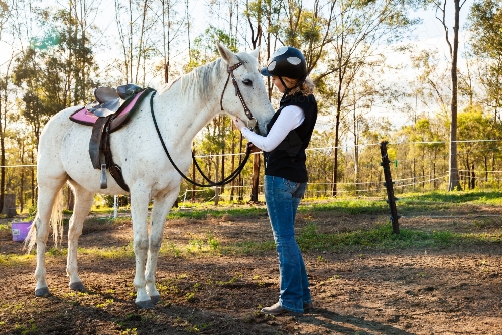 19yo horse rider talking to her horse before going for a ride in paddock - Australian Stock Image
