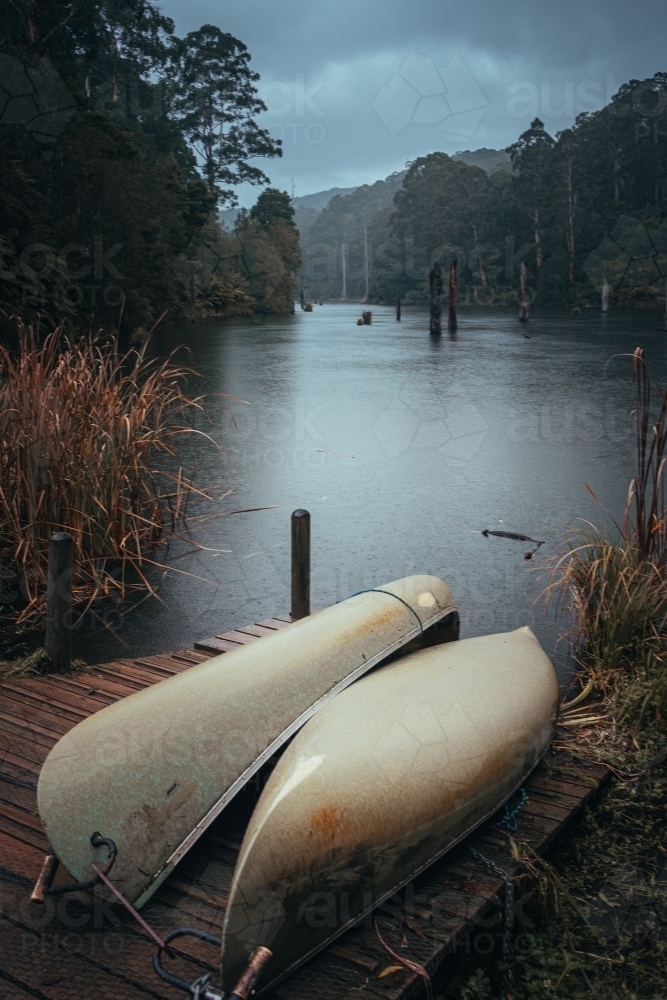 2 Canoes Docked on a Jetty Beside a Remote Lake in the Rain - Australian Stock Image