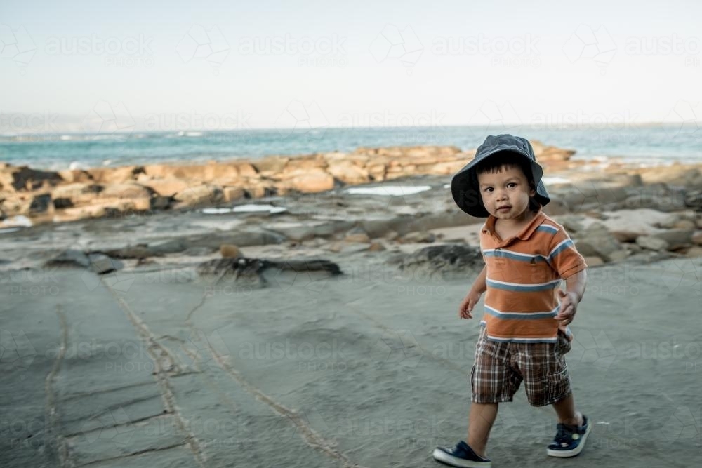 2 year old mixed race boy looks for shells on a rocky coast - Australian Stock Image