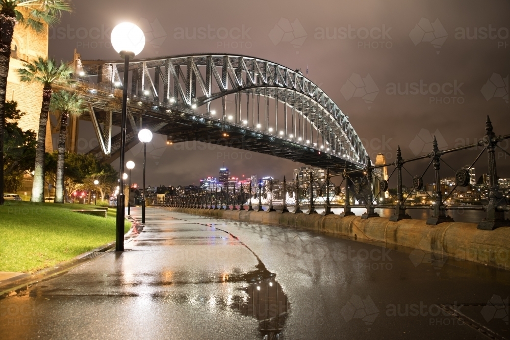 Wet footpath along Sydney Harbour leading to The Sydney Harbour Bridge at night after the rain - Australian Stock Image