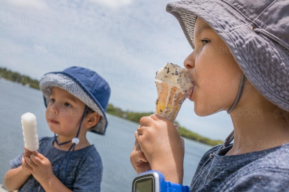 3 and 5 year old mixed race boys eating ice-cream on a warm summer day - Australian Stock Image