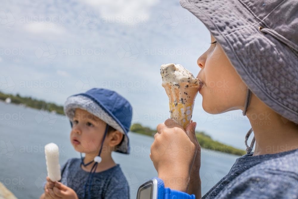 3 and 5 year old mixed race boys eating ice-cream on a warm summer day - Australian Stock Image