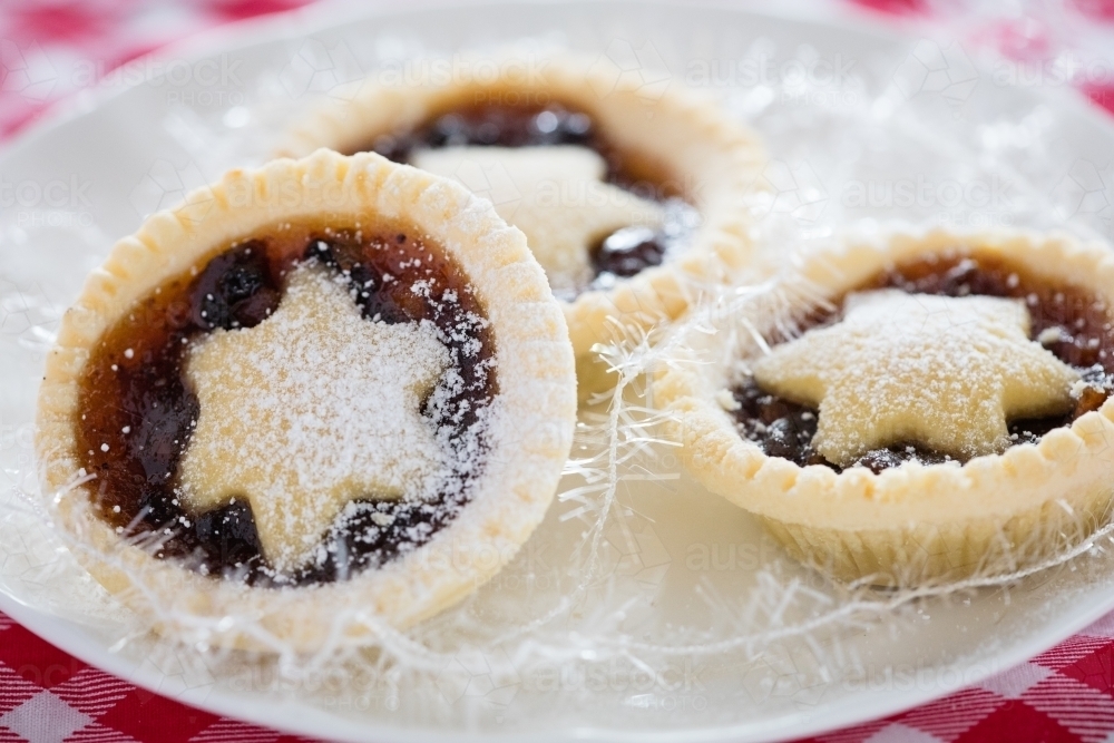 3 fruit mince pies on a white plate on top of a Christmas table cloth - Australian Stock Image