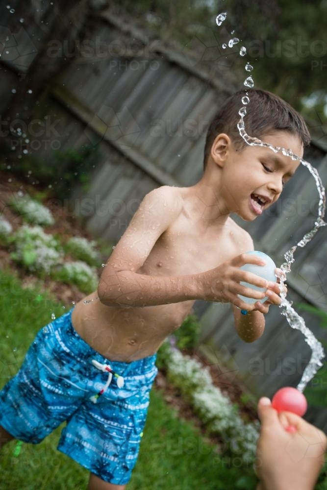 3 year old and 6 year old mixed race brothers play excitedly with water bombs in suburban backyard - Australian Stock Image