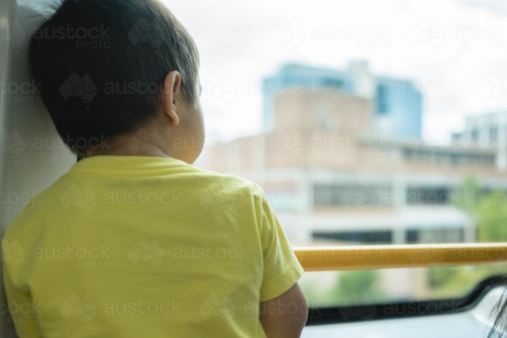 3 year old mixed race boy looks out the window on a Sydney city train - Australian Stock Image