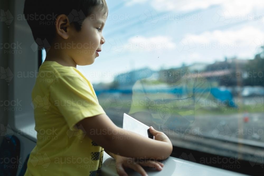3 year old mixed race boy looks out the window while riding on a Sydney city train - Australian Stock Image