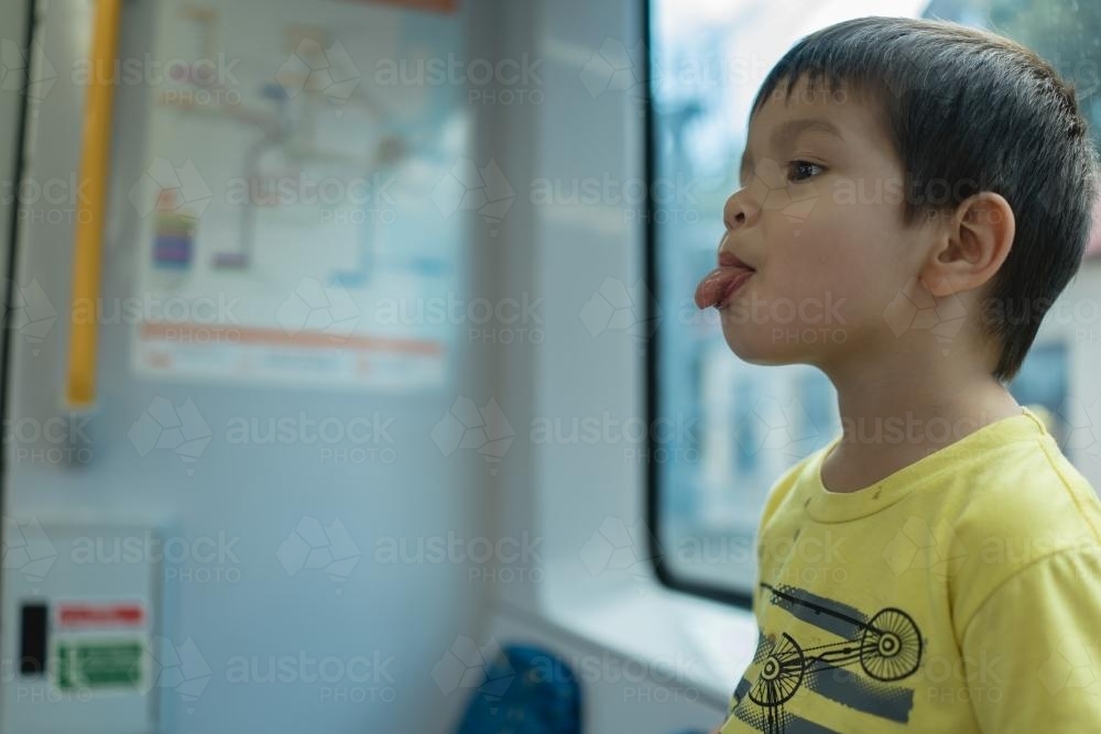 3 year old mixed race boy pokes his tongue out while riding on a Sydney city train - Australian Stock Image