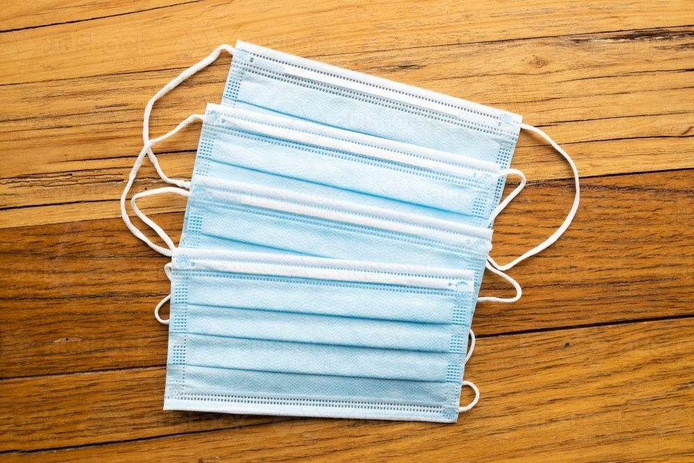 4 blue disposable surgical mask on a wooden background of PPE used during the corona virus COVID-19 - Australian Stock Image