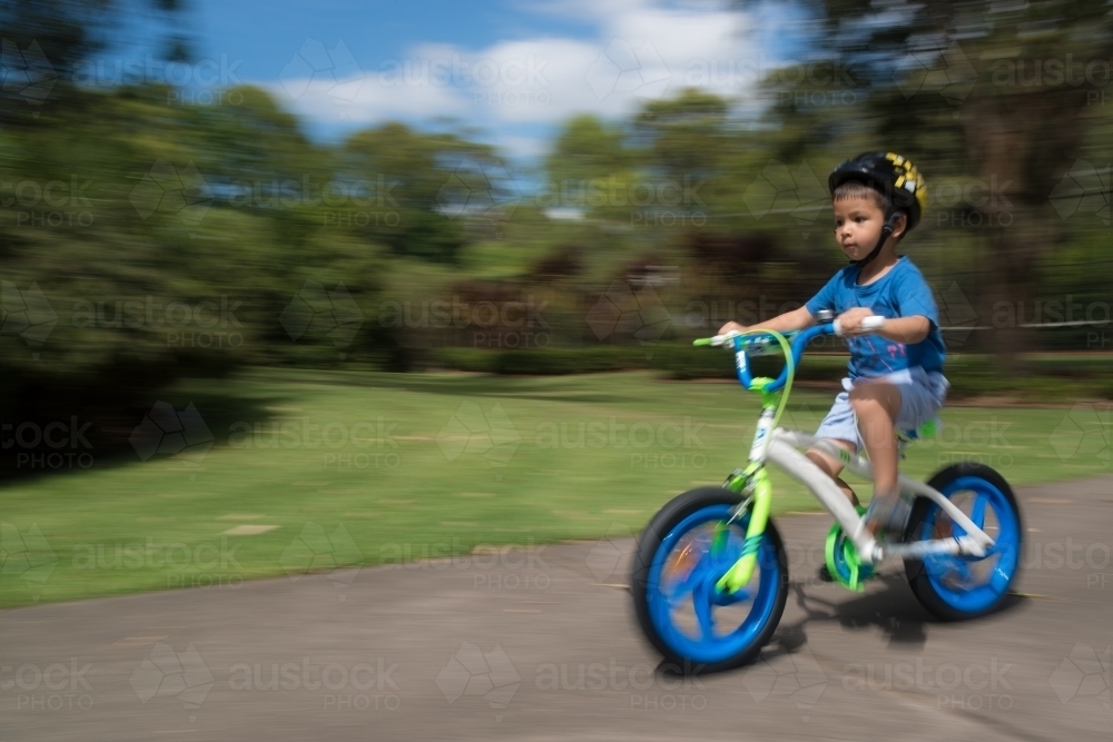 4 year old mixed race boy learns to ride his new bike for the first time. With motion blur - Australian Stock Image