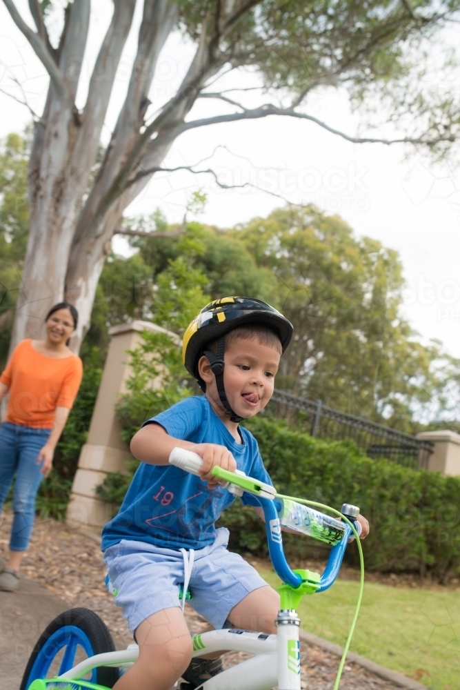 4 year old mixed race boy learns to ride his new bike with Asian mother in background - Australian Stock Image