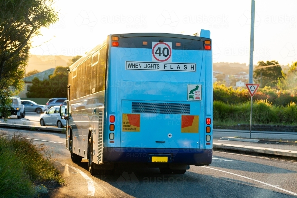 40 when lights flash sign on back of blue bus traveling through urban roundabout - Australian Stock Image