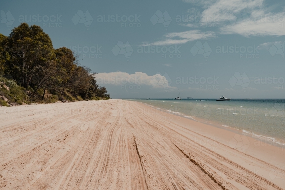 4WD tyre tracks on the beach and clear blue ocean water near Tangalooma - Australian Stock Image