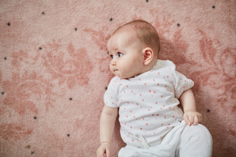 6-month old baby girl enjoying lying on pink carpet - Australian Stock Image