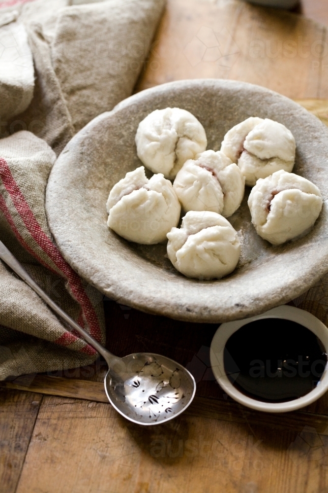 6 small white dough in round shape in a  small bowl with grey  spoon and black sauce - Australian Stock Image