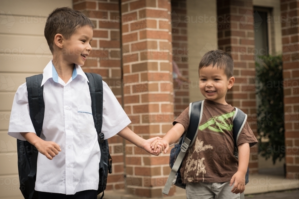 6 year old mixed race boy leaves home with his preschooler brother for his first day of school - Australian Stock Image