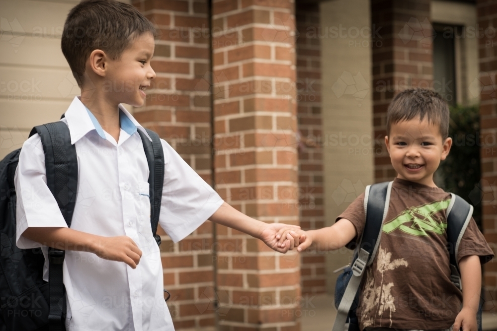 6 year old mixed race boy leaves home with his preschooler brother for his first day of school - Australian Stock Image