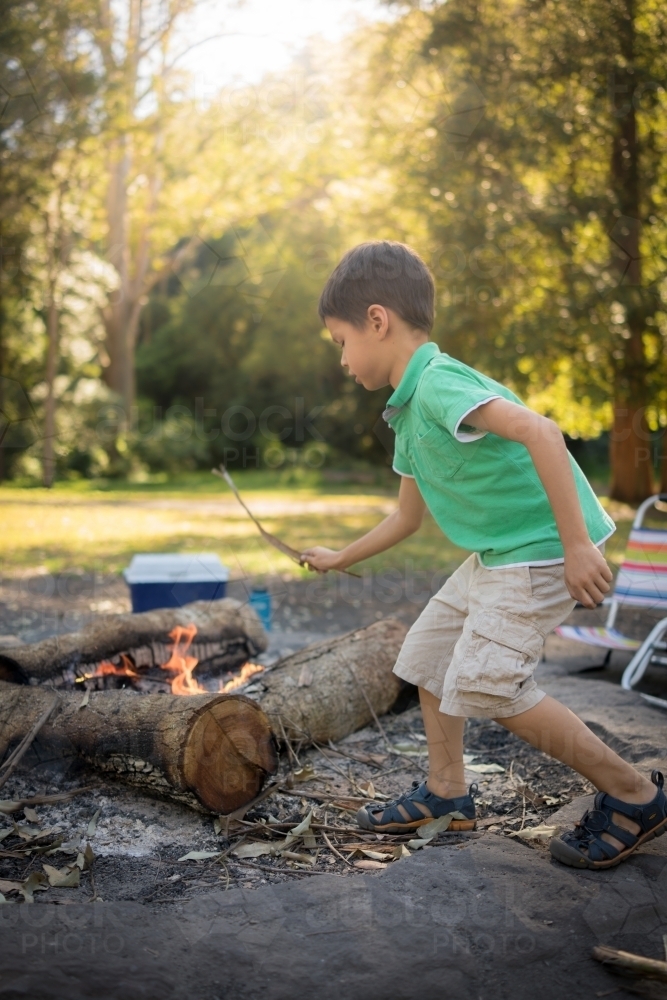 6 year old mixed race boy throws a stick on a camp fire - Australian Stock Image