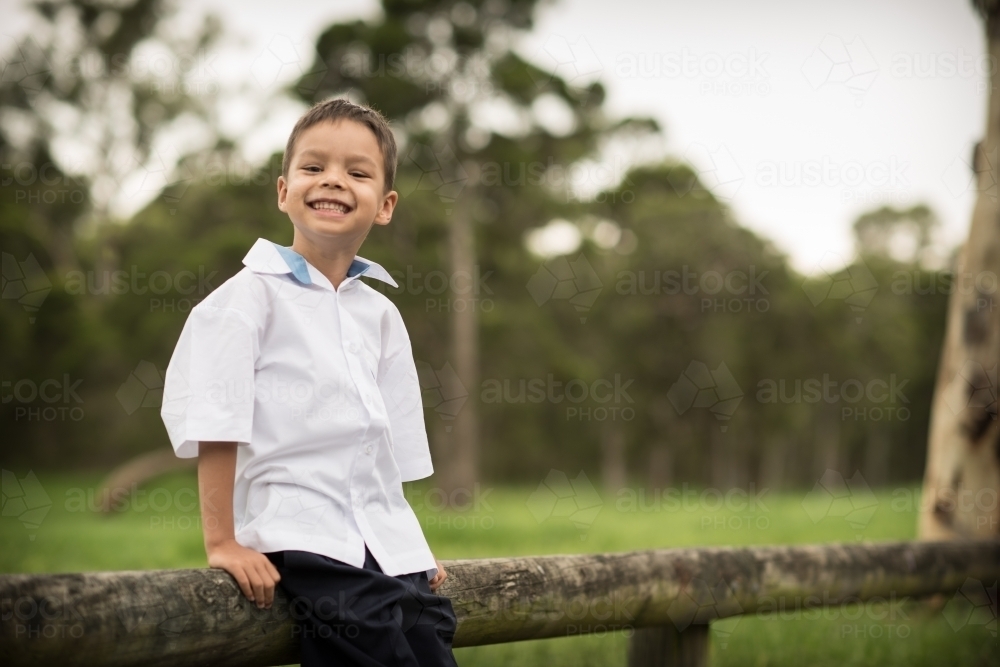 6 year old mixed race boy waits on a road side fence post for his first day of school - Australian Stock Image