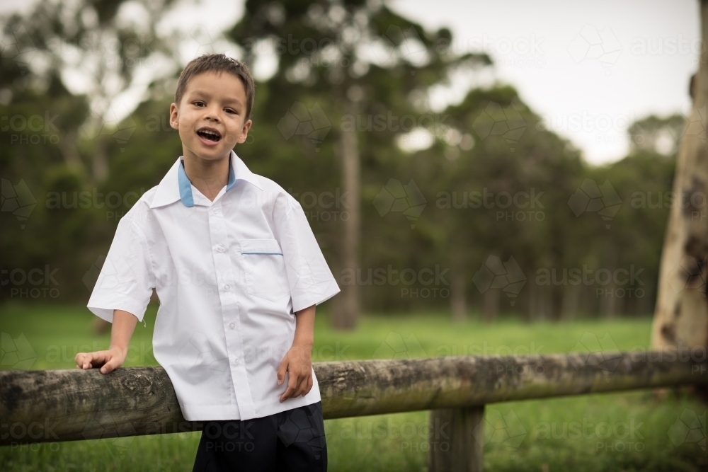 6 year old mixed race boy waits on a road side fence post for his first day of school - Australian Stock Image