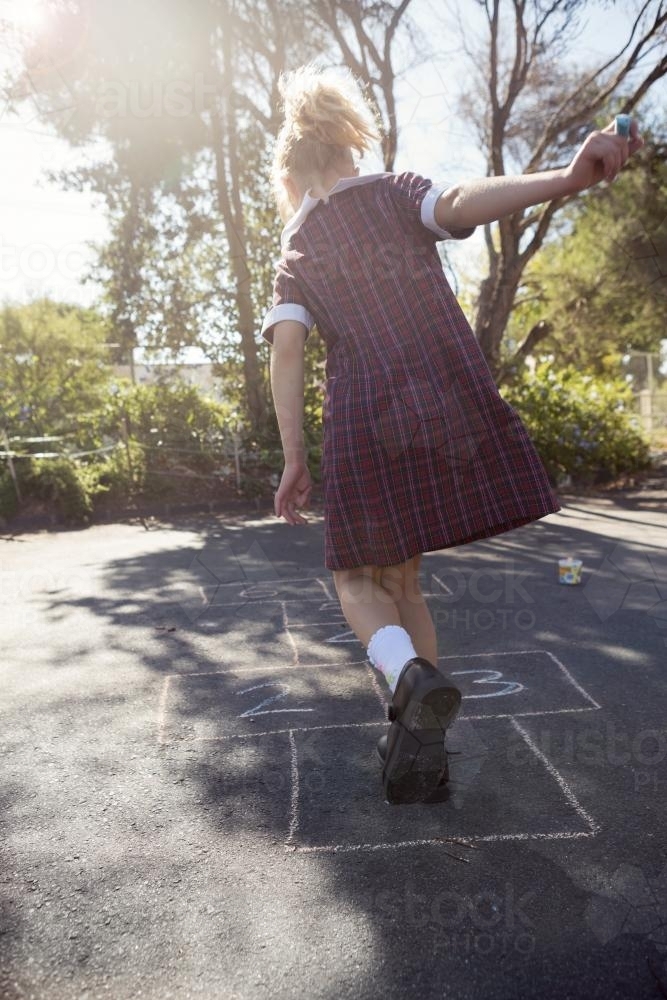 7 year old girl playing hopscotch in school uniform on asphalt - Australian Stock Image