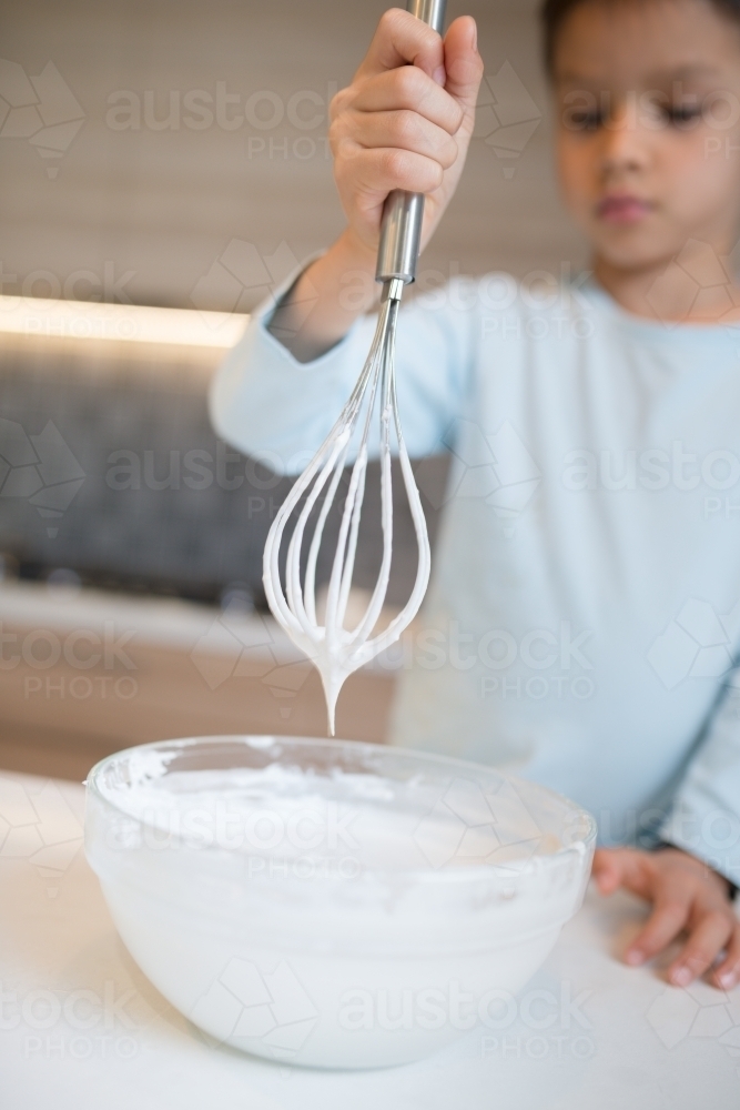 7 year old mixed race boy cooks at home with a whisk and bowl - Australian Stock Image