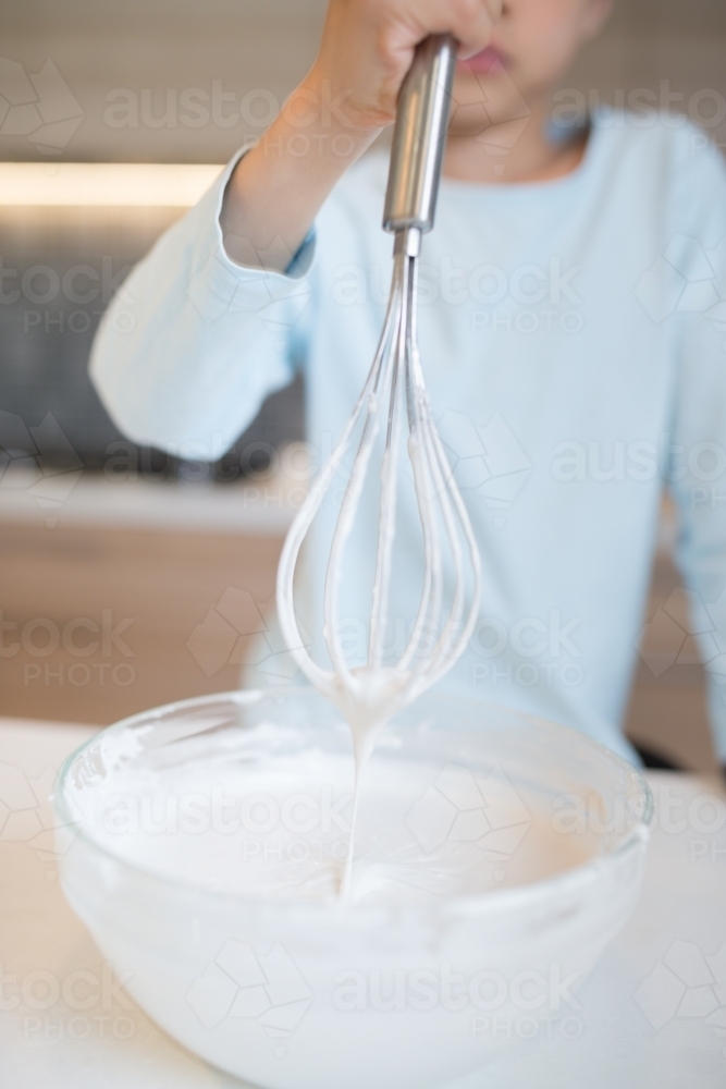 7 year old mixed race boy cooks at home with a whisk and bowl - Australian Stock Image
