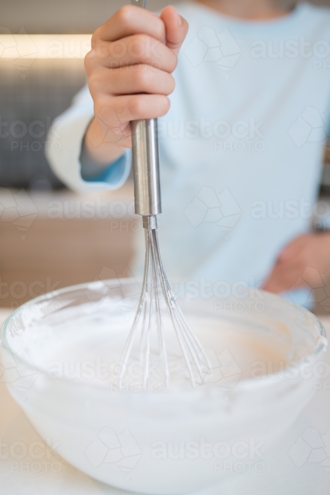 7 year old mixed race boy cooks at home with a whisk and bowl - Australian Stock Image