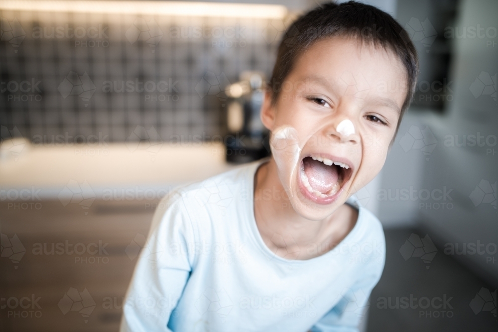 7 year old mixed race boy laughs at the mess he's made on his face while cooking at home - Australian Stock Image
