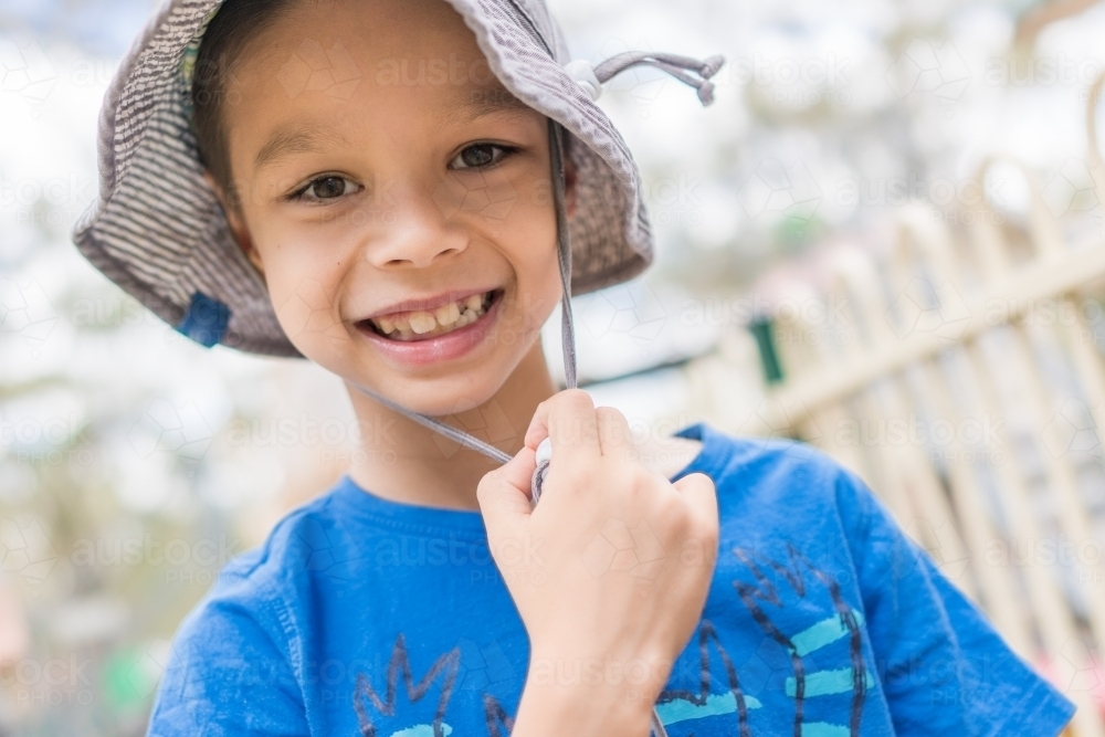 7 year old mixed race boy smiling and wearing a hat outside - Australian Stock Image