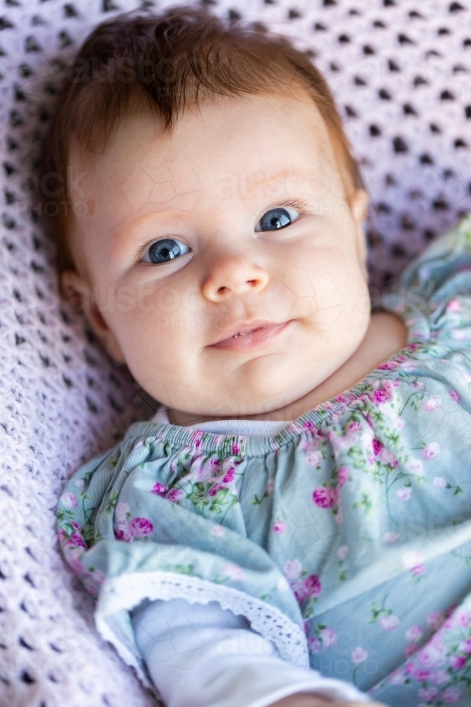 9 week old baby with wide eyes looking at camera sitting in bouncer on crocheted blanket - Australian Stock Image