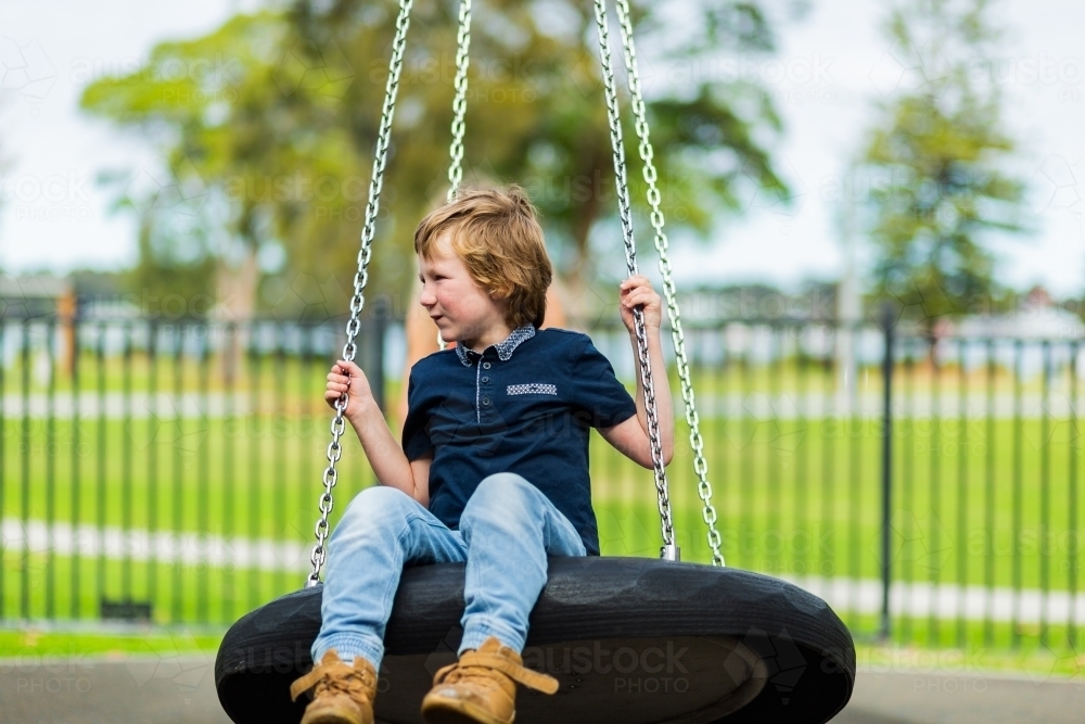 9yo boy outdoors on a swing at the park - Australian Stock Image
