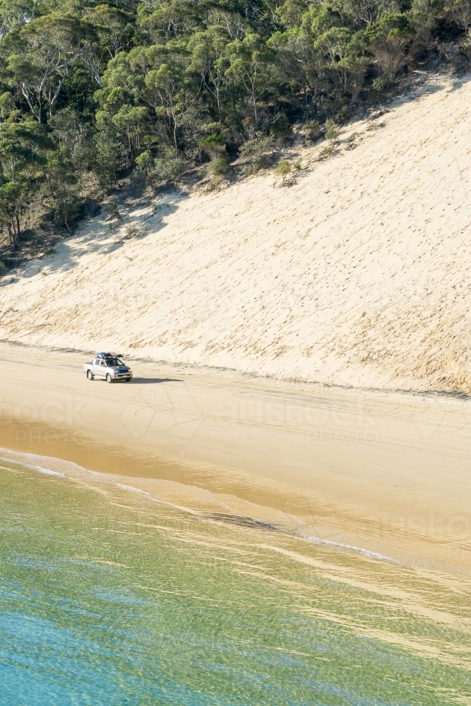 A 4WD driving along a beach below a sand dune - Australian Stock Image