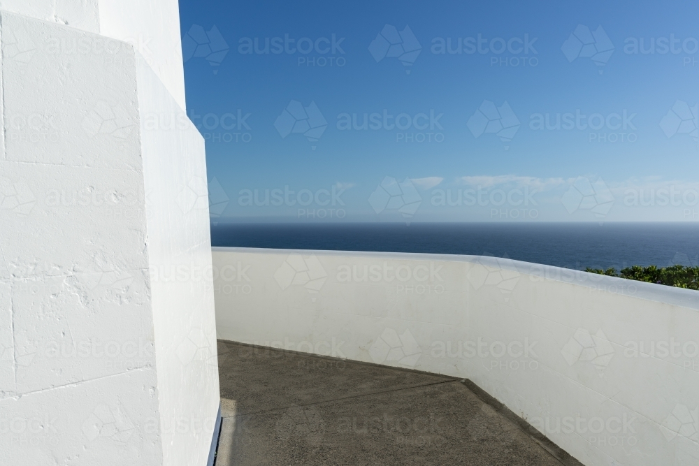A balcony with a white balustrade, overlooking a serene sea under a clear blue sky. - Australian Stock Image