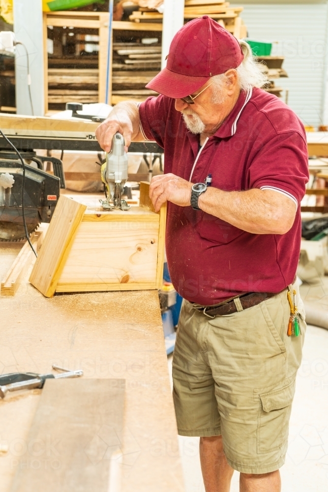 A bearded handyman cutting a hole in a wooden bird box in a Men's shed - Australian Stock Image