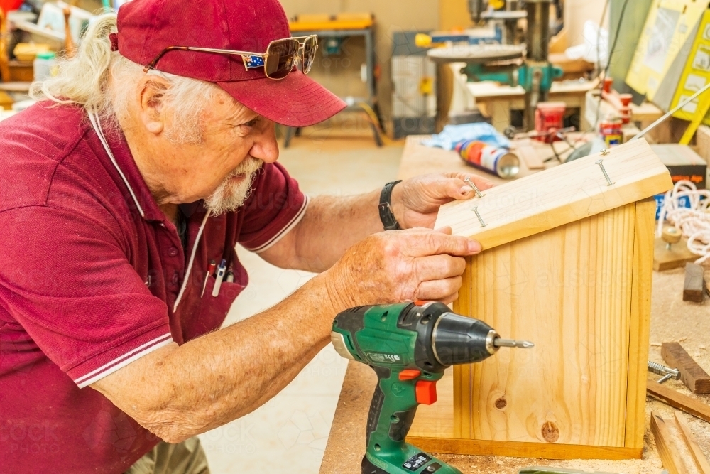 A bearded handyman fitting the lid to a wooden birdbox in a Men's shed - Australian Stock Image