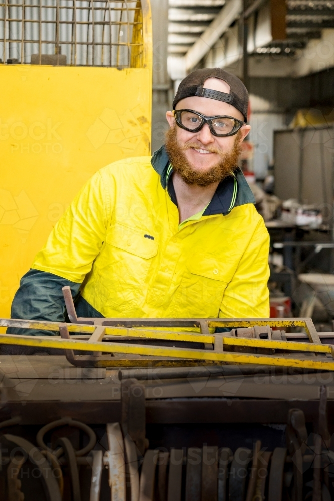 A bearded tradesman smiling over the top of a workbench - Australian Stock Image