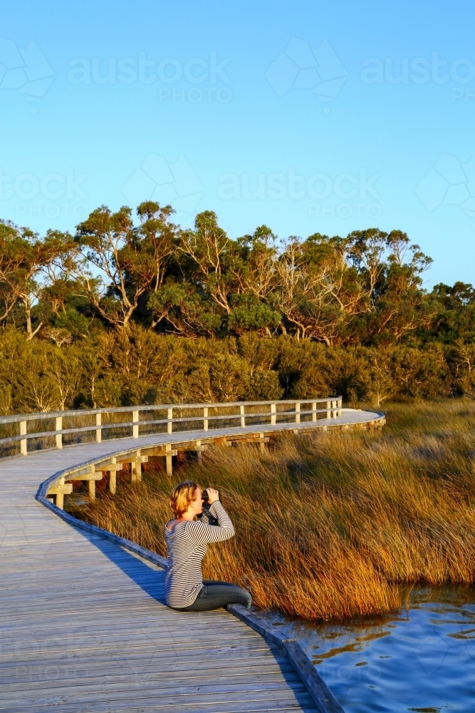 A blonde lady in her 30's scouts for birds using her binoculars on an observation deck - Australian Stock Image