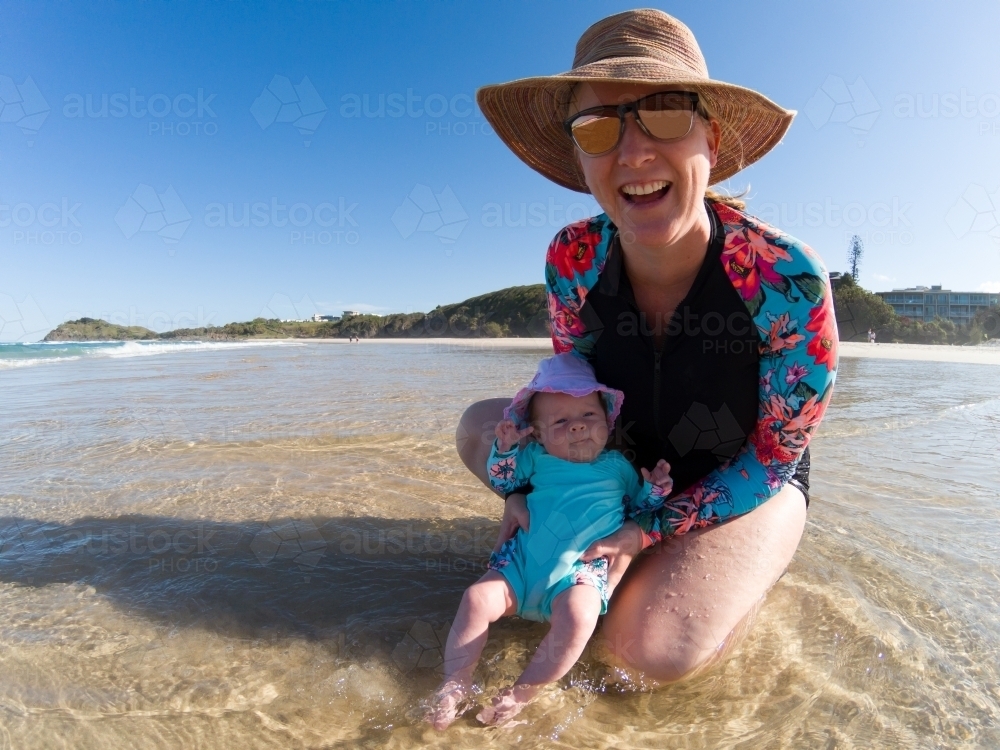A blonde mum in her late thirties with baby playing at beach. - Australian Stock Image