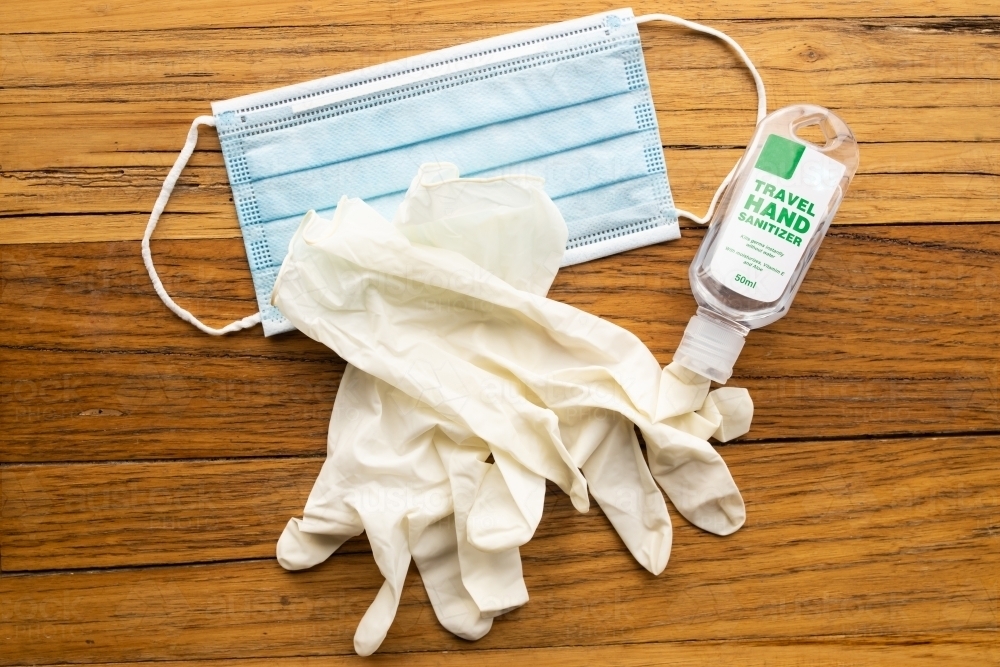 A blue disposable mask, cream disposable latex gloves and travel sized hand sanitizer - Australian Stock Image