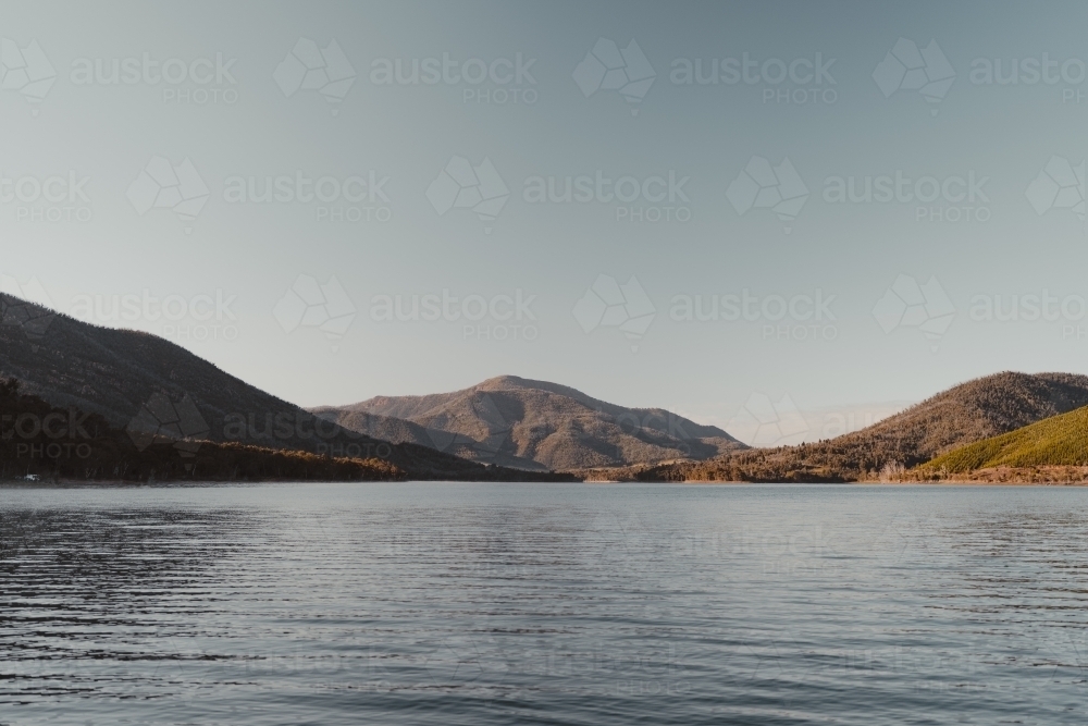 A blue lake with mountains in the background after sunrise - Australian Stock Image