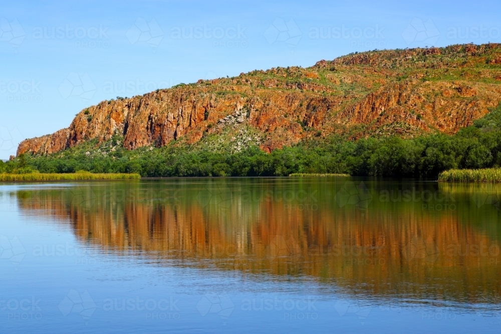 A bluff is reflected on the calm water of Lake Kununurra - Australian Stock Image