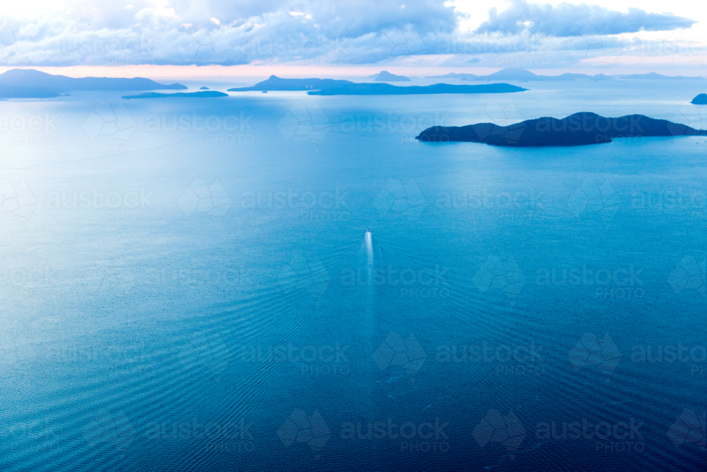 A boat leaves a long white wake across calm blue water at dusk - Australian Stock Image