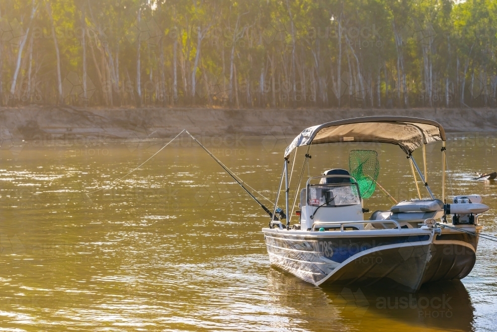 A boat sitting on a river with a fishing rod resting over the side - Australian Stock Image