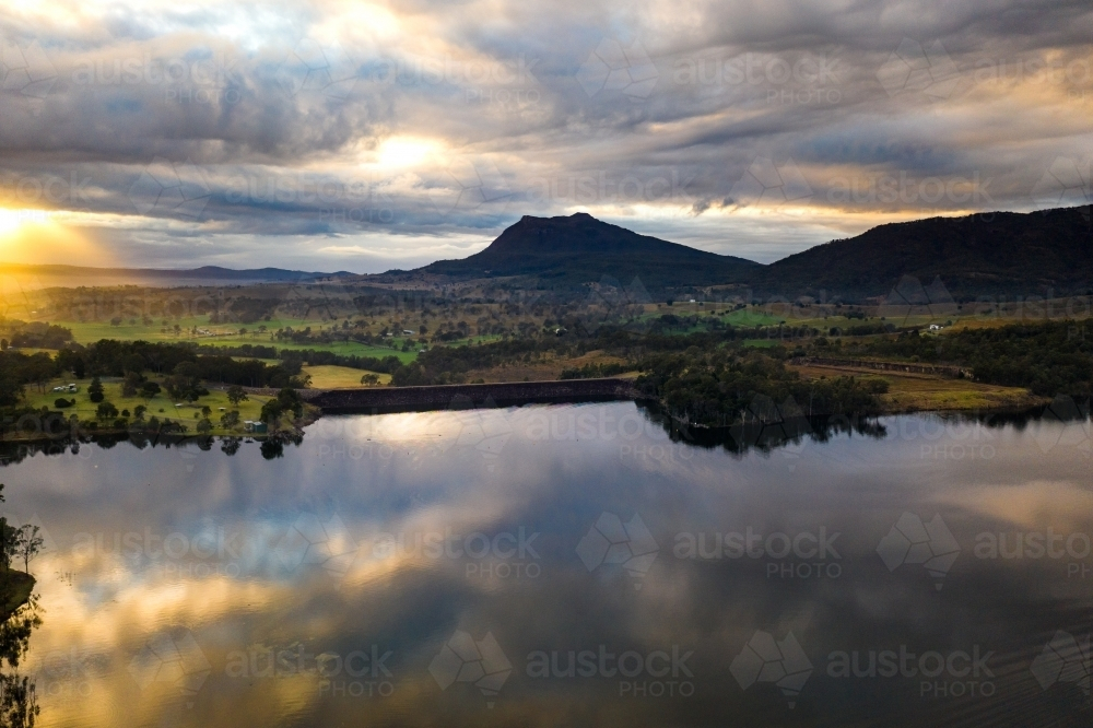 A body of water mirrors clouds in an overcast sky with mountain on horizon - Australian Stock Image