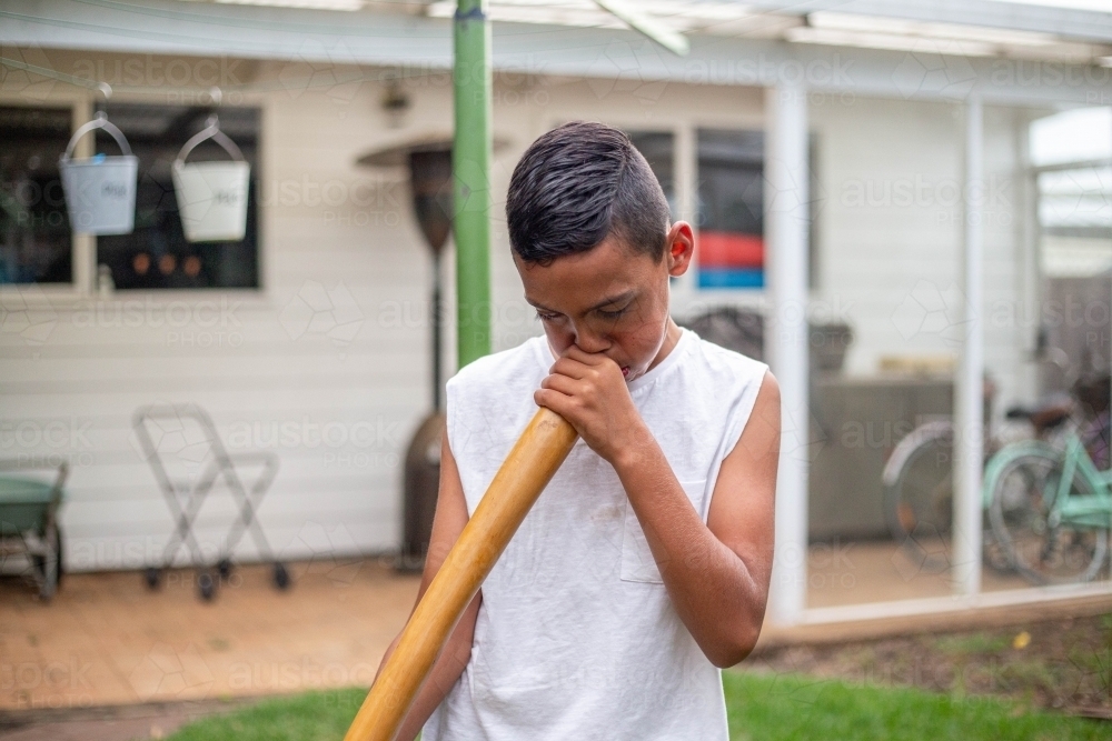 a boy in a white shirt blowing on a didgeridoo - Australian Stock Image