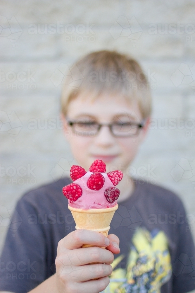 A boy looking at his ice-cream covered in raspberries - Australian Stock Image